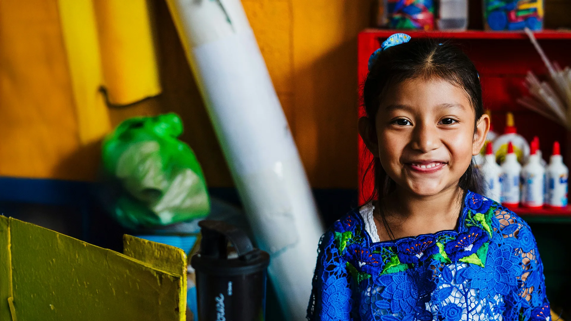 Una niña sonriente con blusa bordada en un salón de clases