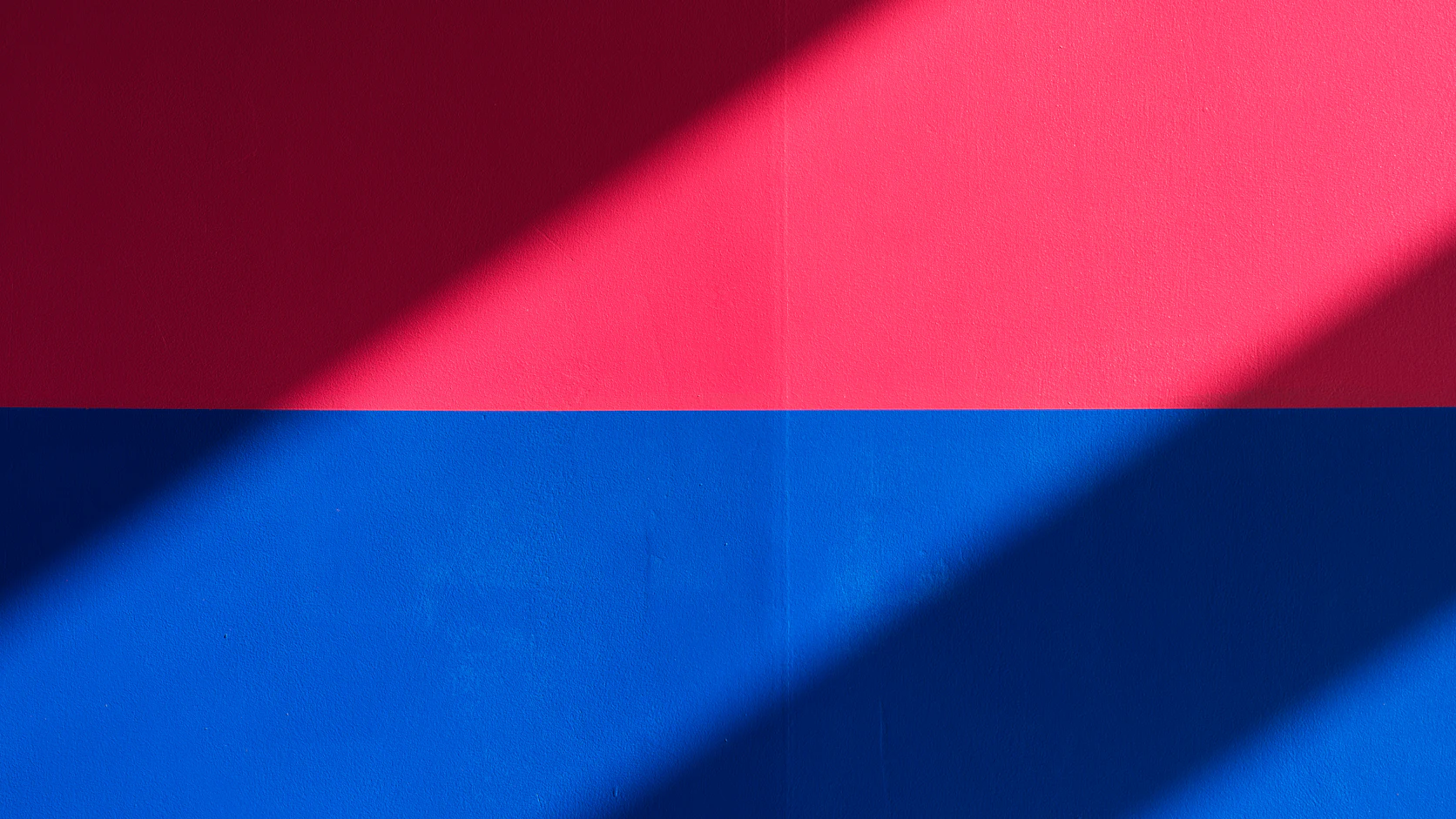 A wall painted red above and blue below, crossed by a diagonal band of shadow