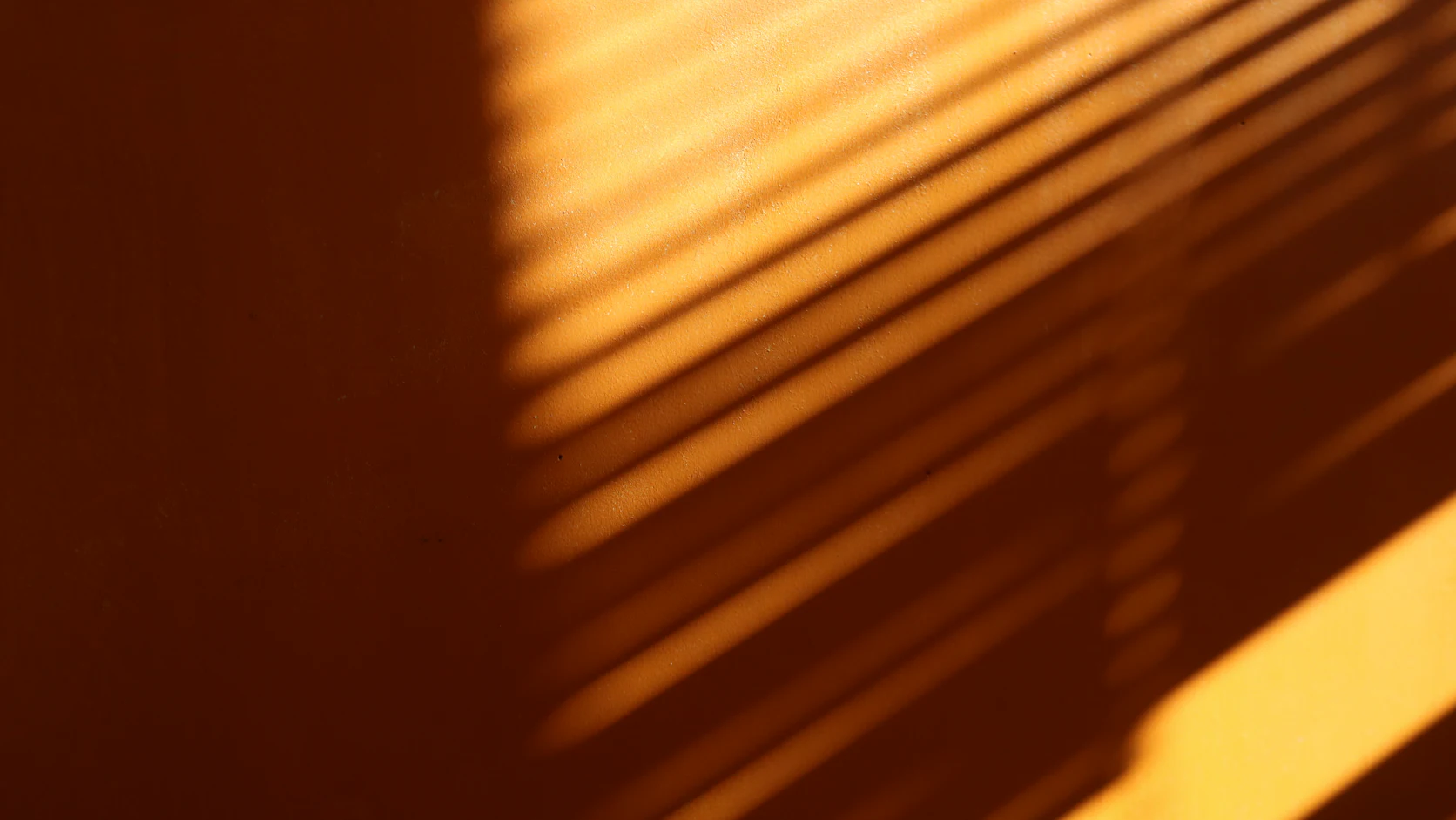 Sunlight through blinds casting stripes across an orange wall