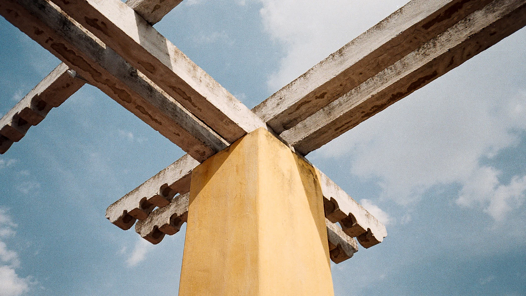 Crossed beams above a yellow column against a blue sky