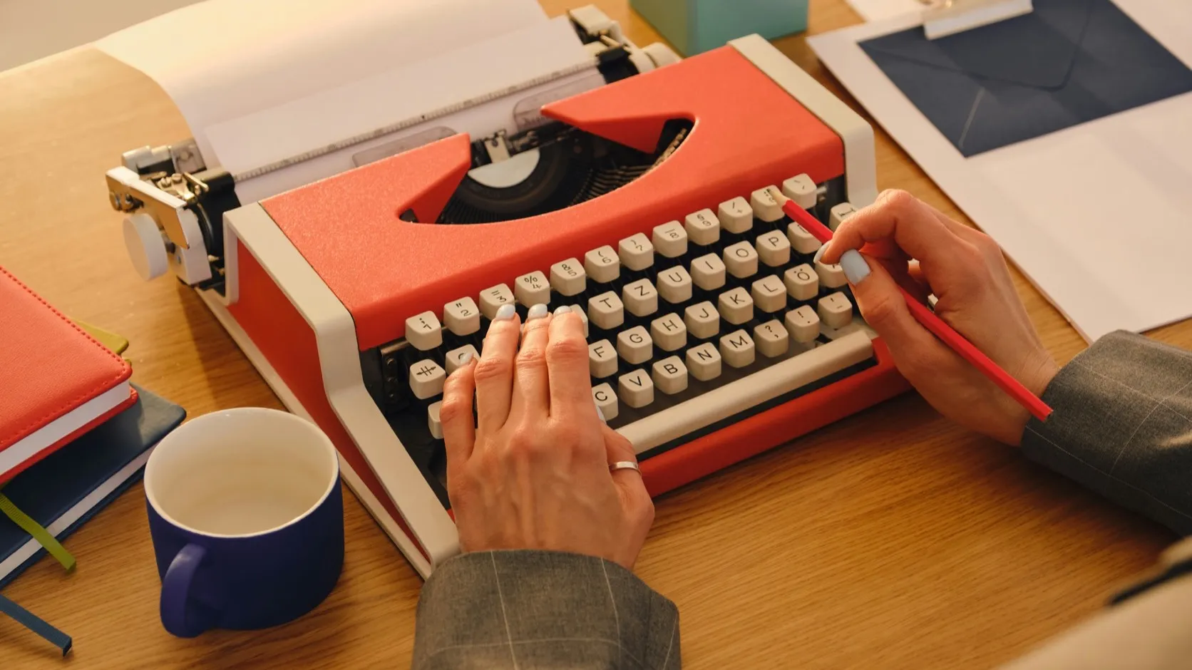 Hands typing on a red vintage typewriter on a wooden desk