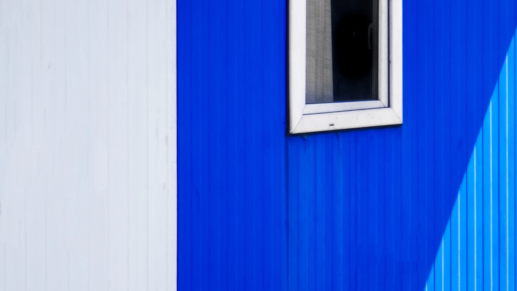 A cobalt blue wall beside a white one, with a single window