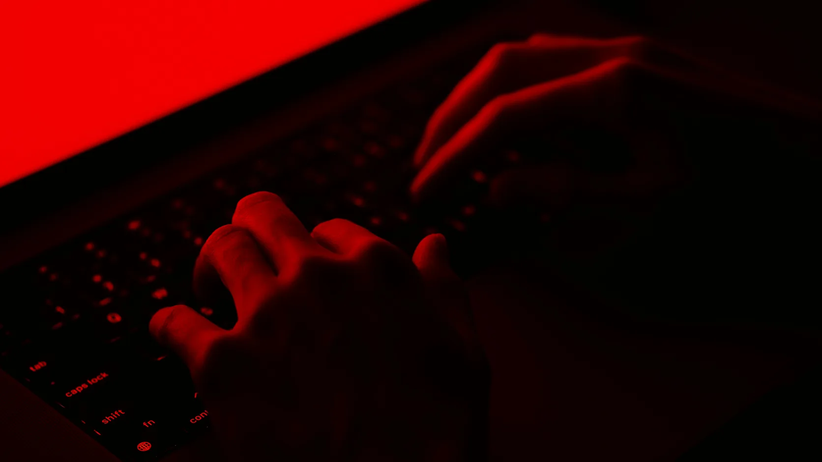 Hands on a laptop keyboard under harsh red light